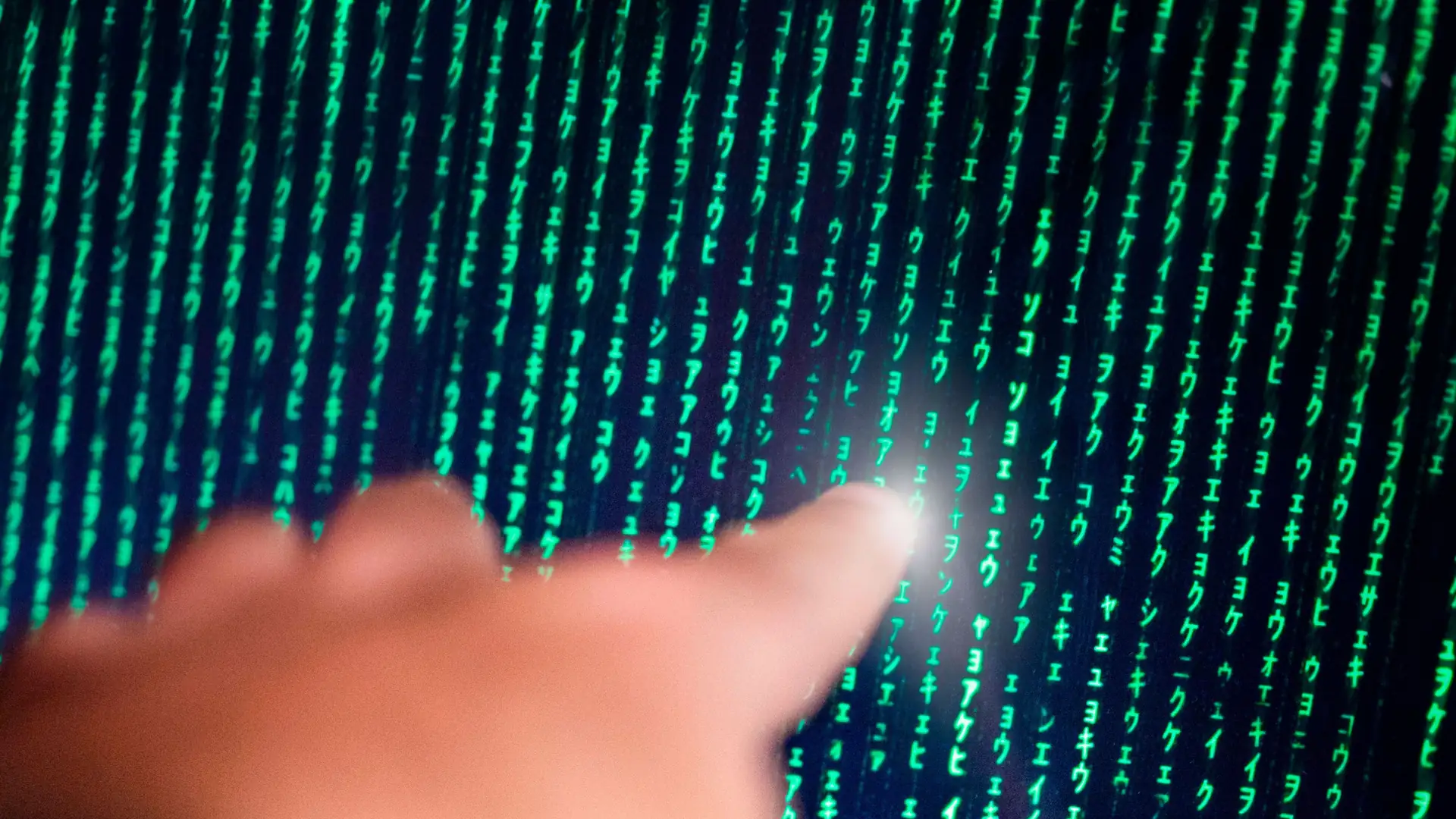 Close-up of a fingertip touching a screen displaying scrolling green code